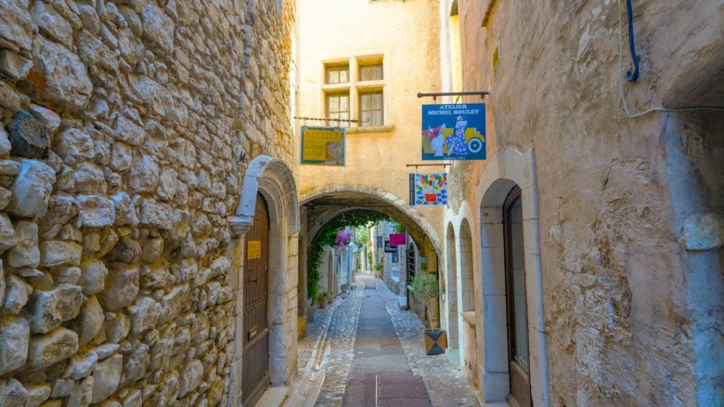 A narrow, ancient stone alleyway with arches and shop signs.