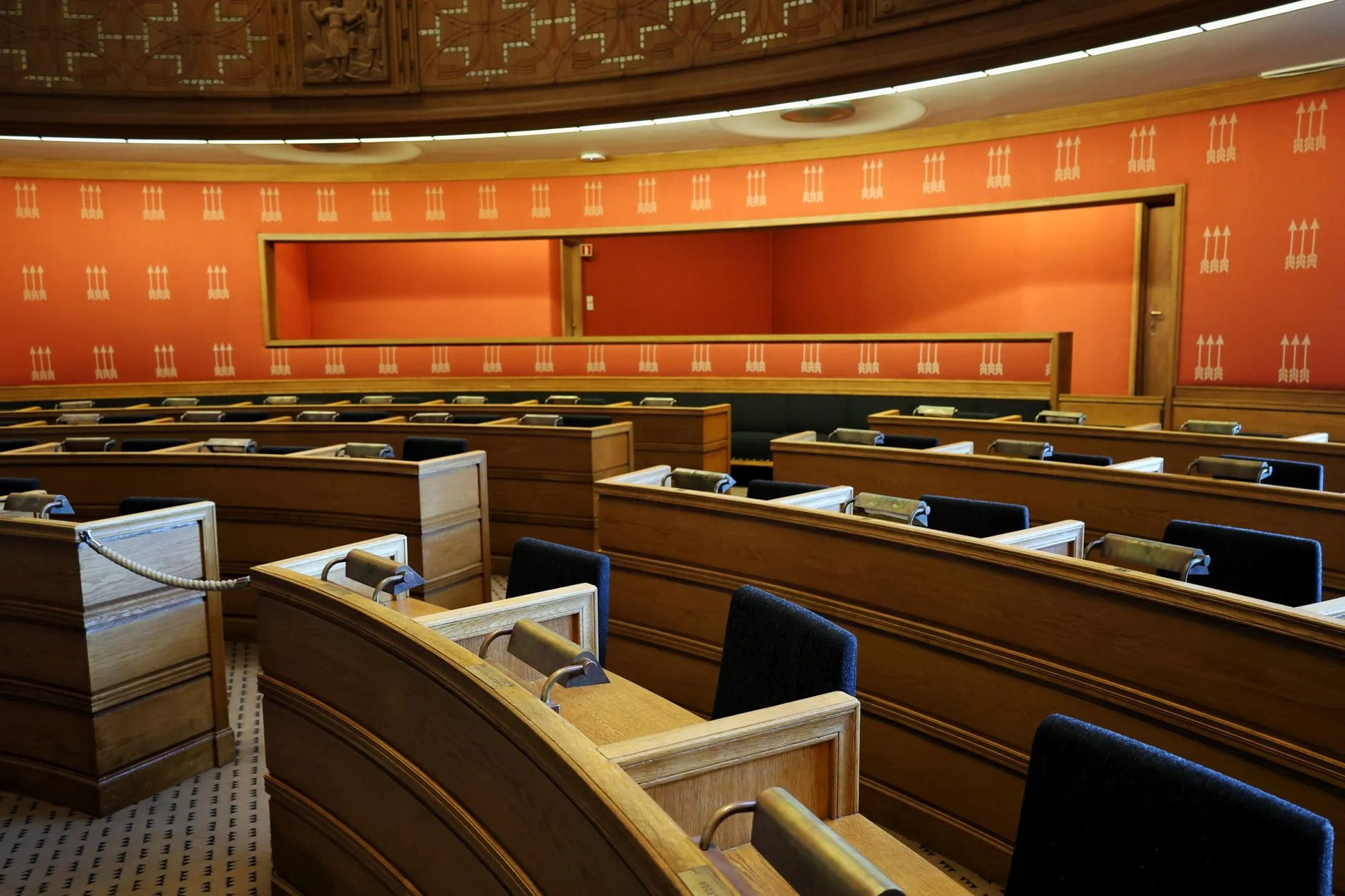 An empty parliamentary meeting room with wooden seating and vibrant orange walls in Oslo, Norway.