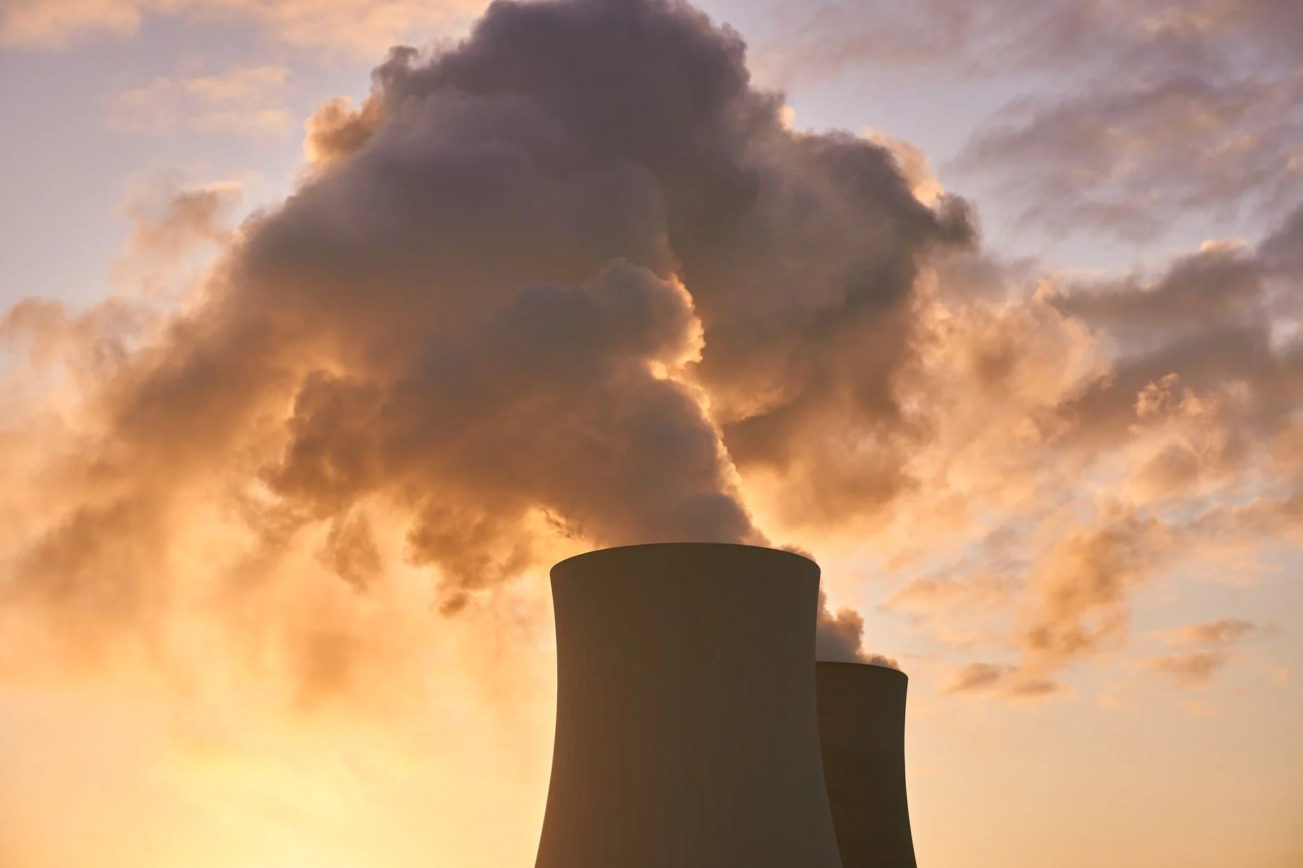 Cooling towers release smoke into a dramatic sunset sky, highlighting environmental impact.