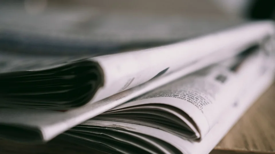 Stack of folded newspapers on a wooden table with a focus on printed pages.