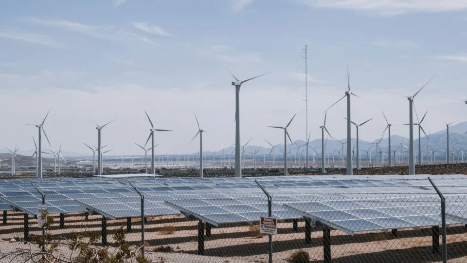 A renewable energy farm with wind turbines and solar panels under a clear sky.