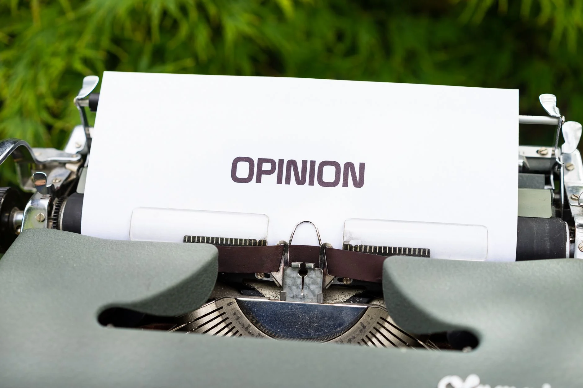 Close-up of a typewriter with paper showing the word 'Opinion' outdoors.