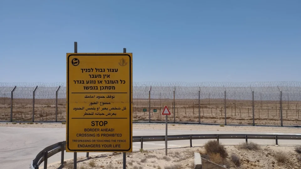 A warning sign prohibiting crossing near a desert border area with clear blue sky.