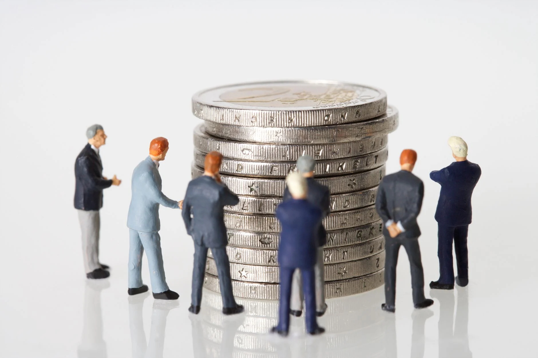 Miniature figurines of businessmen surround a stacked pile of coins on a clean white background.