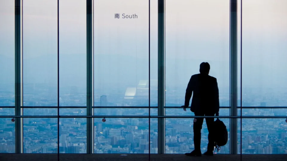 A lone businessman overlooking the city from a high-rise building during day.
