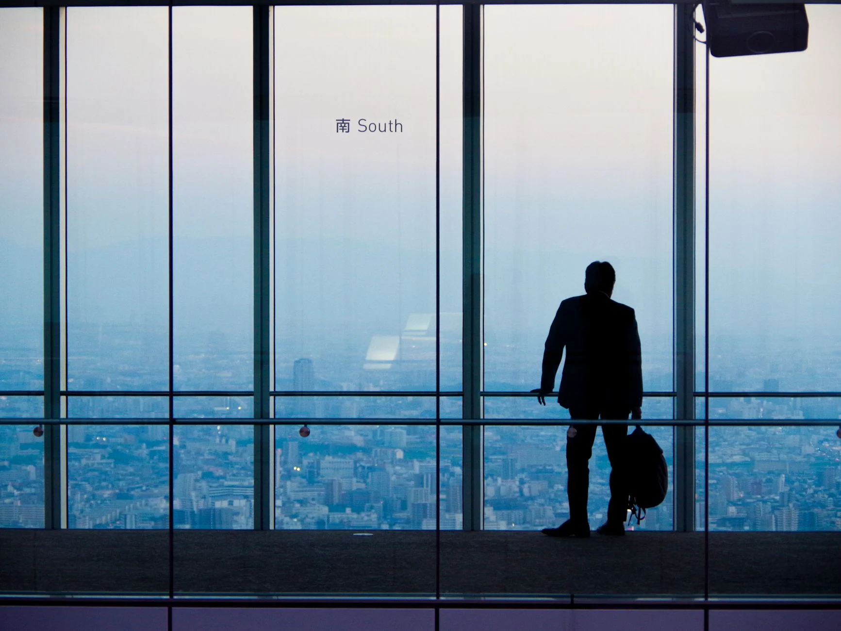 A lone businessman overlooking the city from a high-rise building during day.