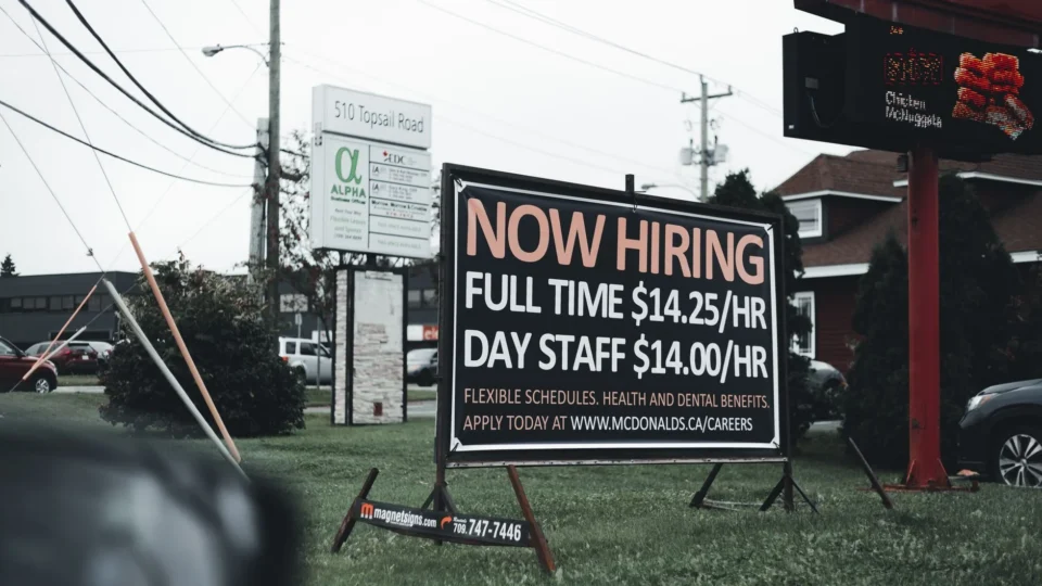 Outdoor hiring sign advertising restaurant job openings with competitive wages and benefits.