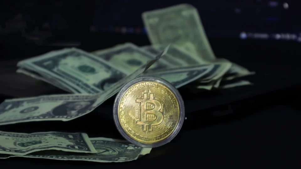 Bitcoin coin surrounded by scattered US dollar bills on a dark surface, symbolizing modern finance.