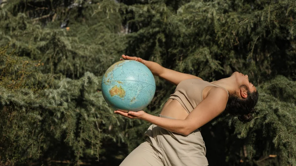 A woman poses with a globe in a forest, symbolizing global environmental awareness.