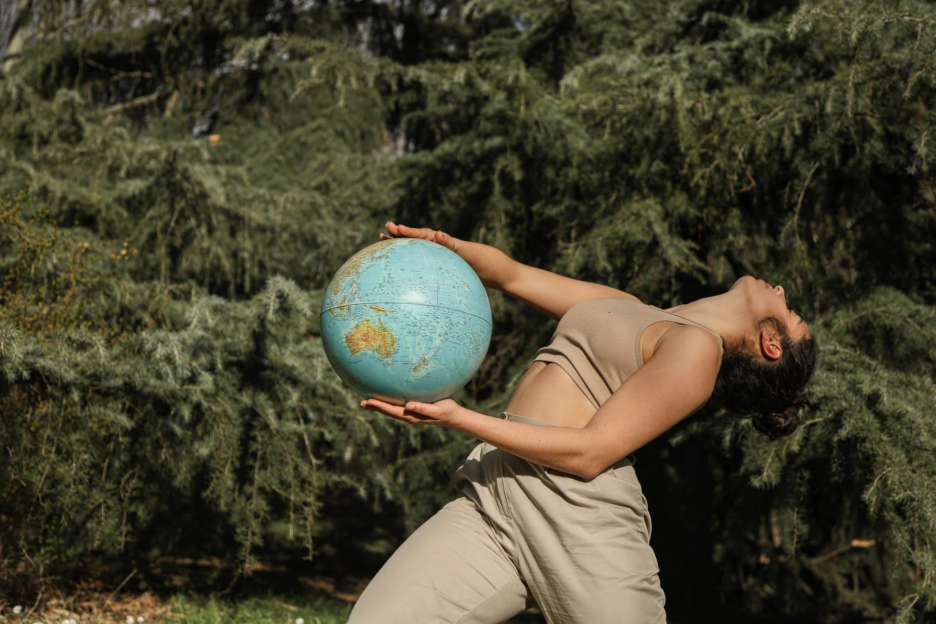 A woman poses with a globe in a forest, symbolizing global environmental awareness.