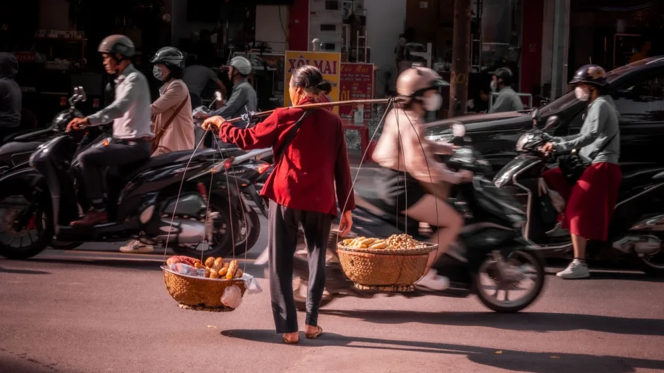 A street vendor balancing baskets amidst bustling traffic on a Hanoi street.