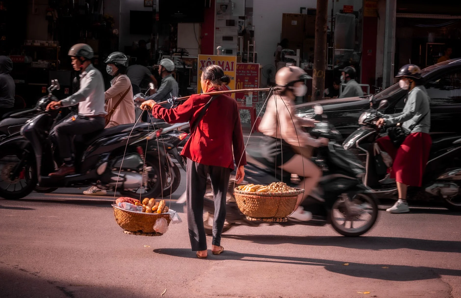 A street vendor balancing baskets amidst bustling traffic on a Hanoi street.
