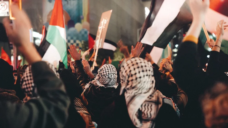 Protest in city street with people holding flags and signs, expressing political views.