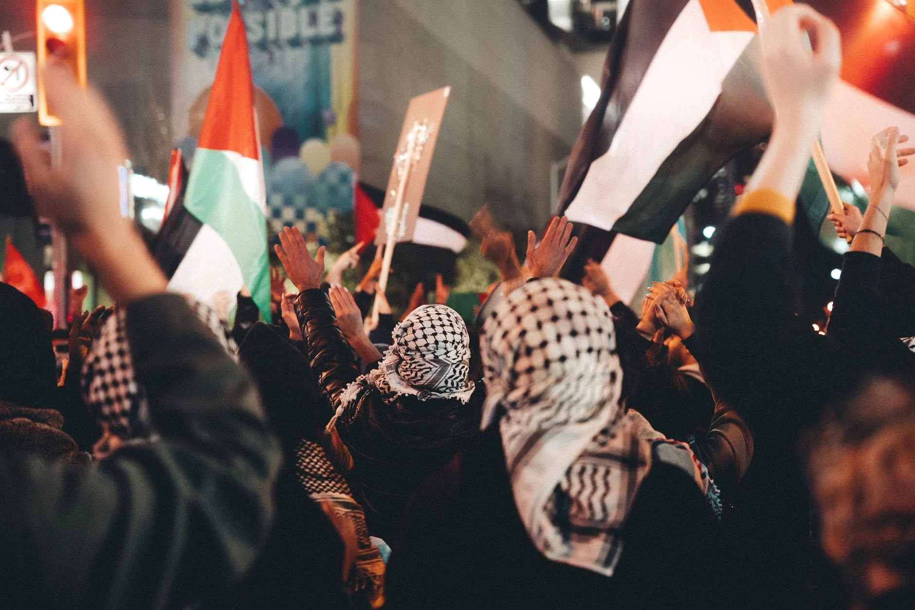 Protest in city street with people holding flags and signs, expressing political views.
