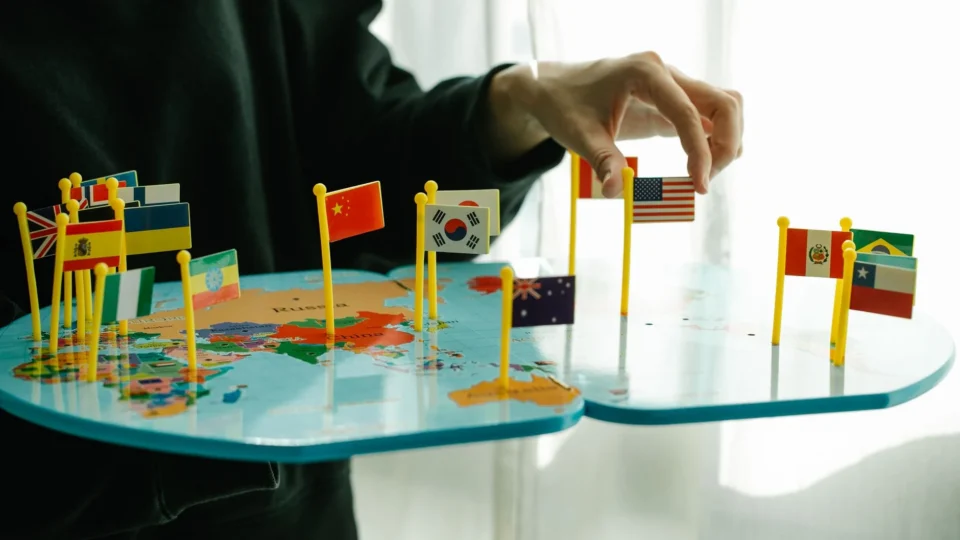 Hand arranging flags on a world map, signifying global diversity.