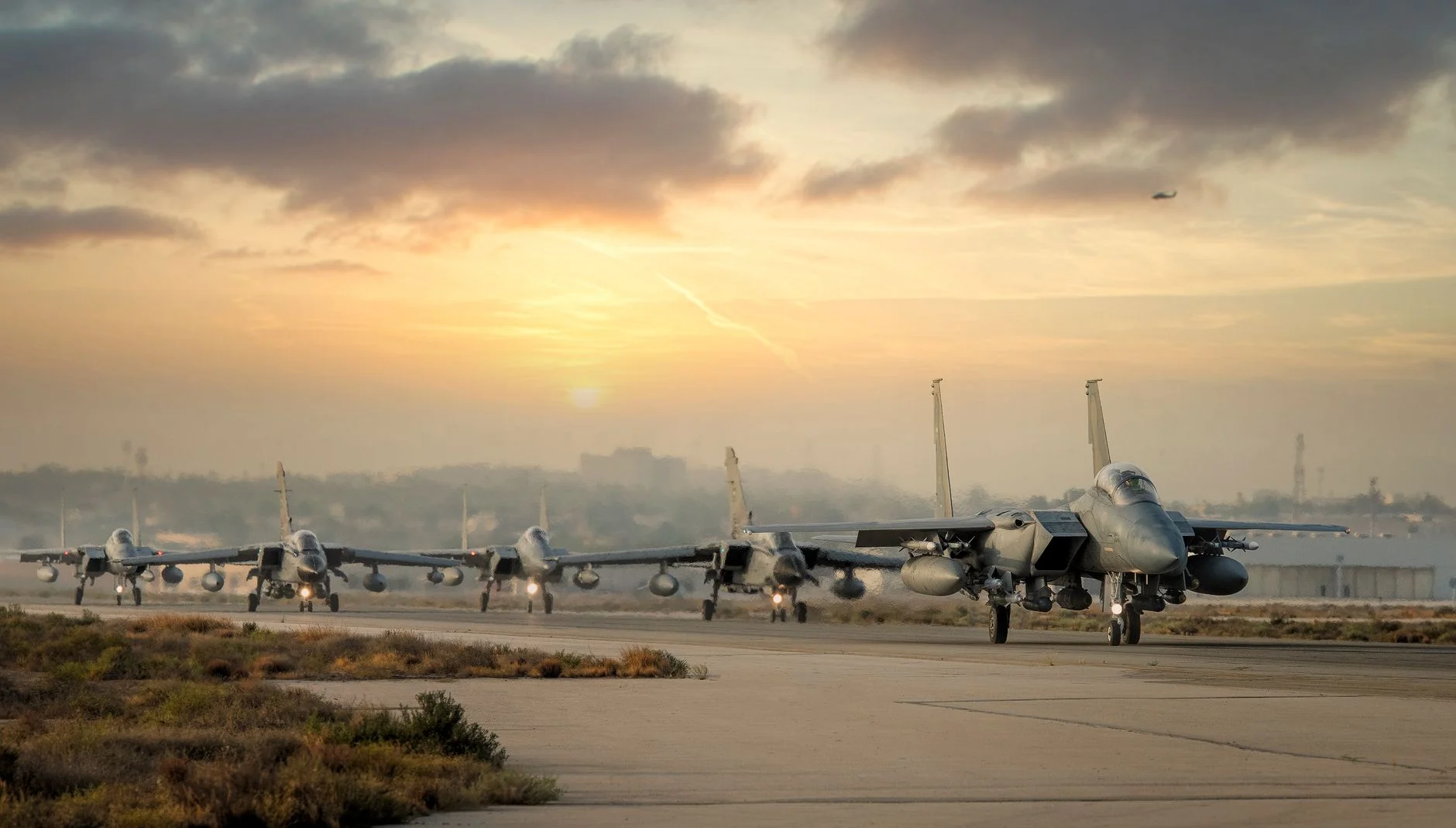 Line of military fighter jets ready for takeoff during a scenic sunset.