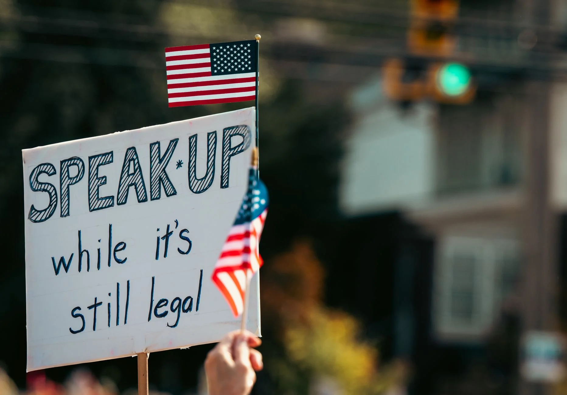 Protest sign with the message and American flag at a rally, highlighting free speech themes.