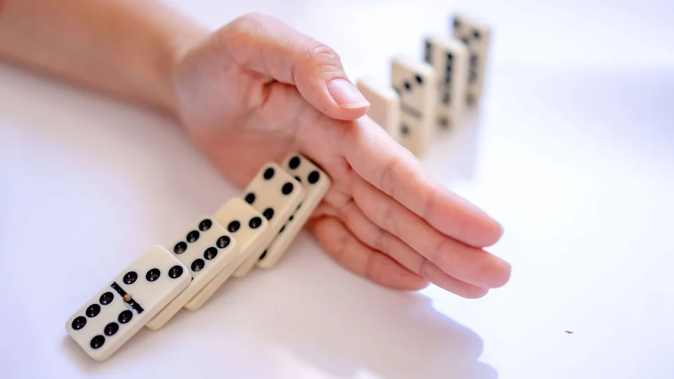 A hand stopping the domino effect, captured on a white background, symbolizing control.