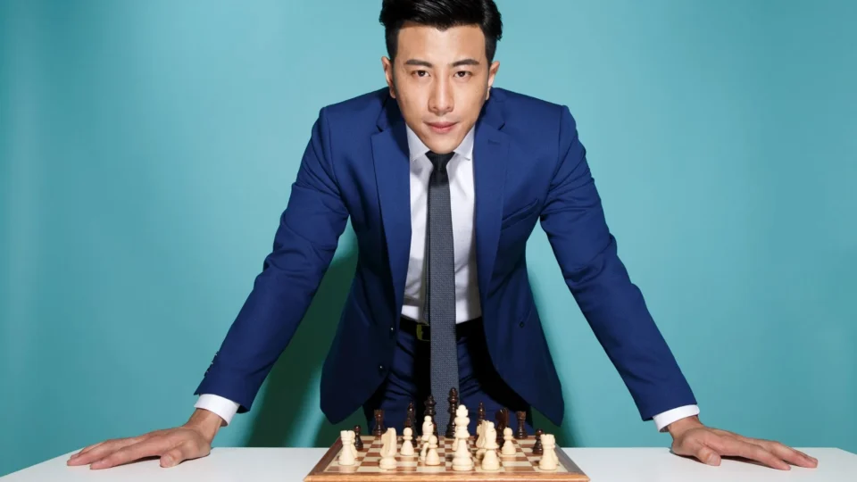 Confident businessman in blue suit strategizing over a chess game, symbolizing business strategy and decision making.