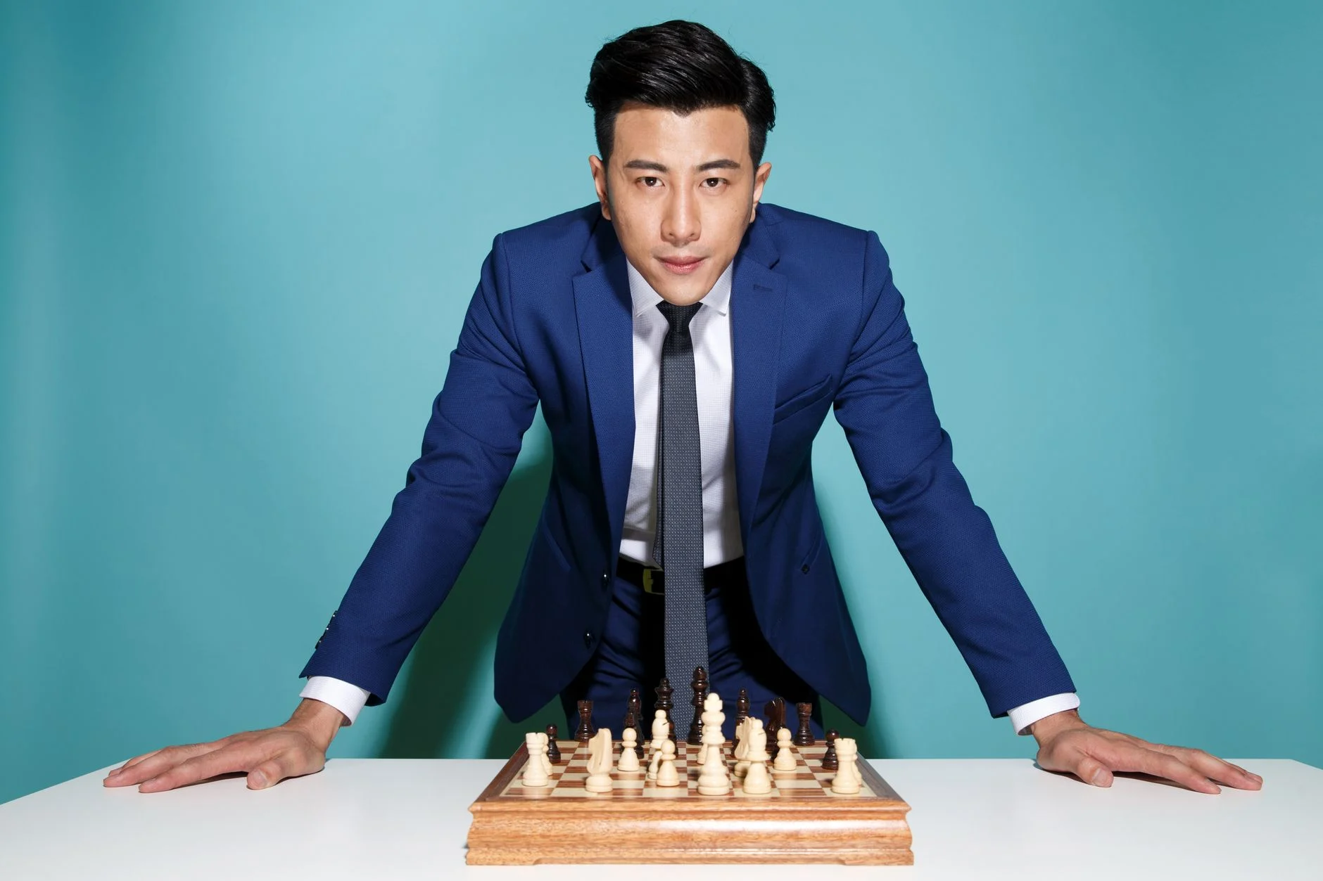 Confident businessman in blue suit strategizing over a chess game, symbolizing business strategy and decision making.