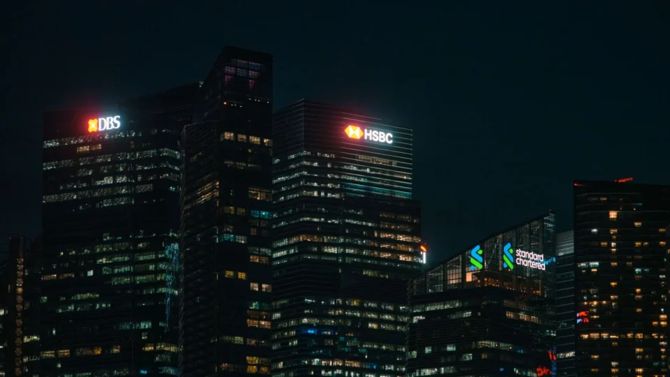 Illuminated city skyscrapers of major banks in Singapore's financial district at night.