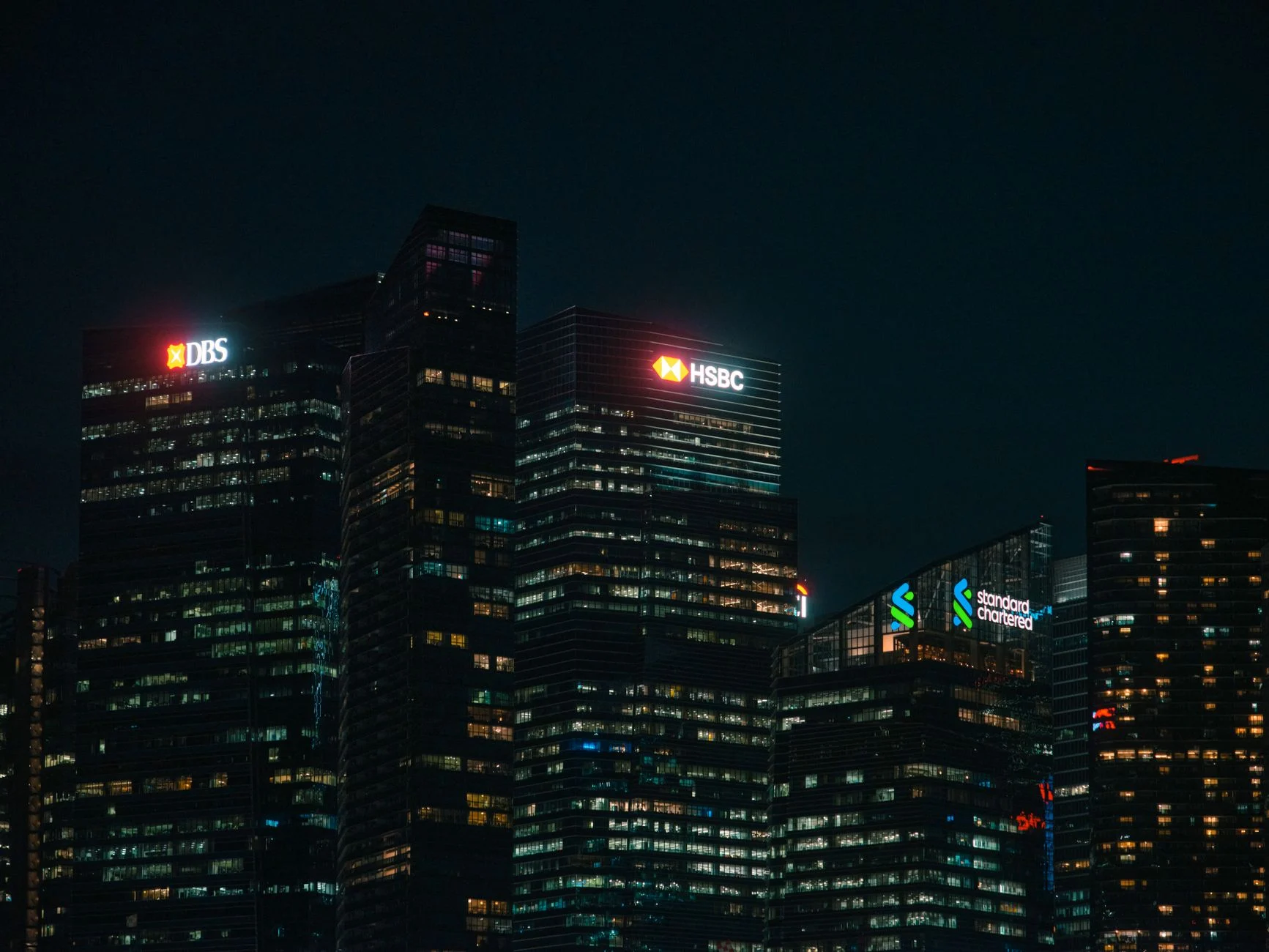 Illuminated city skyscrapers of major banks in Singapore's financial district at night.
