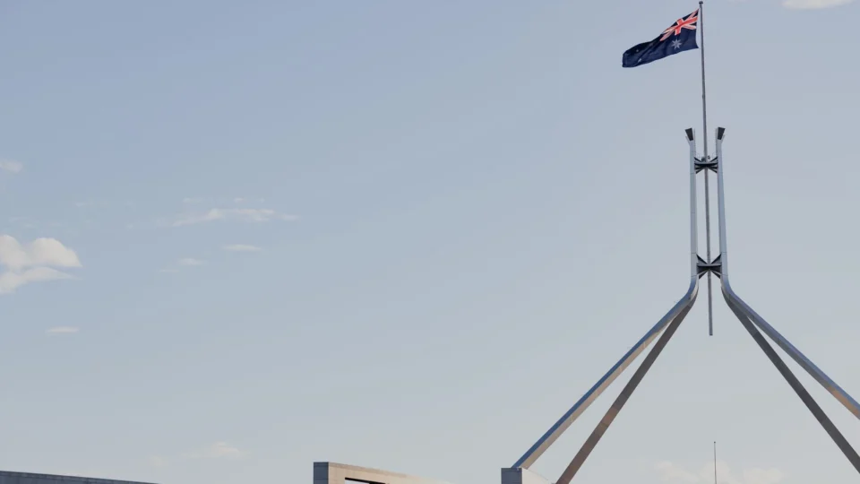 Canberra's iconic Australian Parliament House with national flag against a clear blue sky.