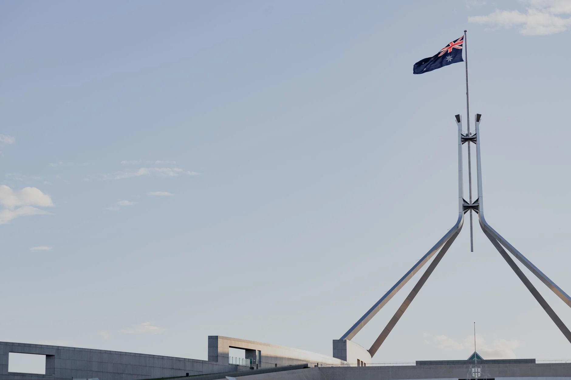 Canberra's iconic Australian Parliament House with national flag against a clear blue sky.