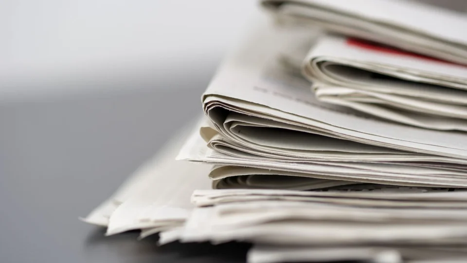 Close-up of stacked newspapers on a table, representing media and journalism.