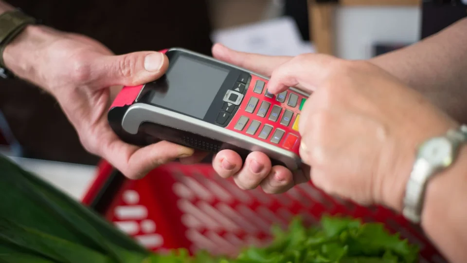 Two people making a cashless payment at a grocery store with a credit card terminal.