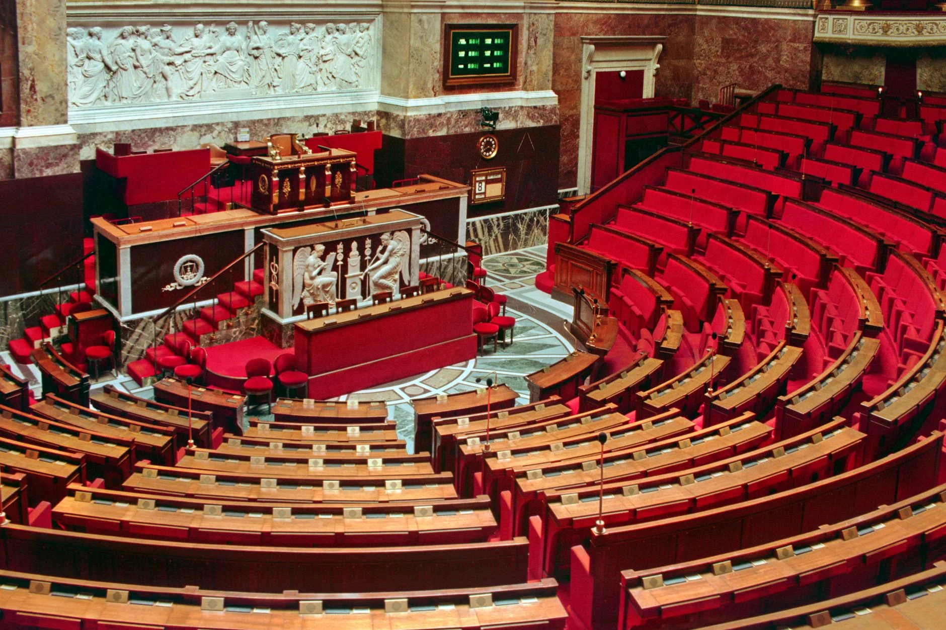 Bright and elegant view of the French National Assembly's rich interior with red seats and ornate decor.