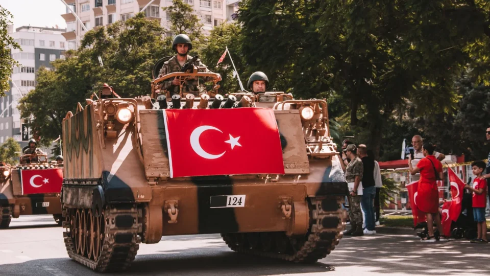 Military tanks in a Turkish parade displaying the national flag and soldiers on a city street.