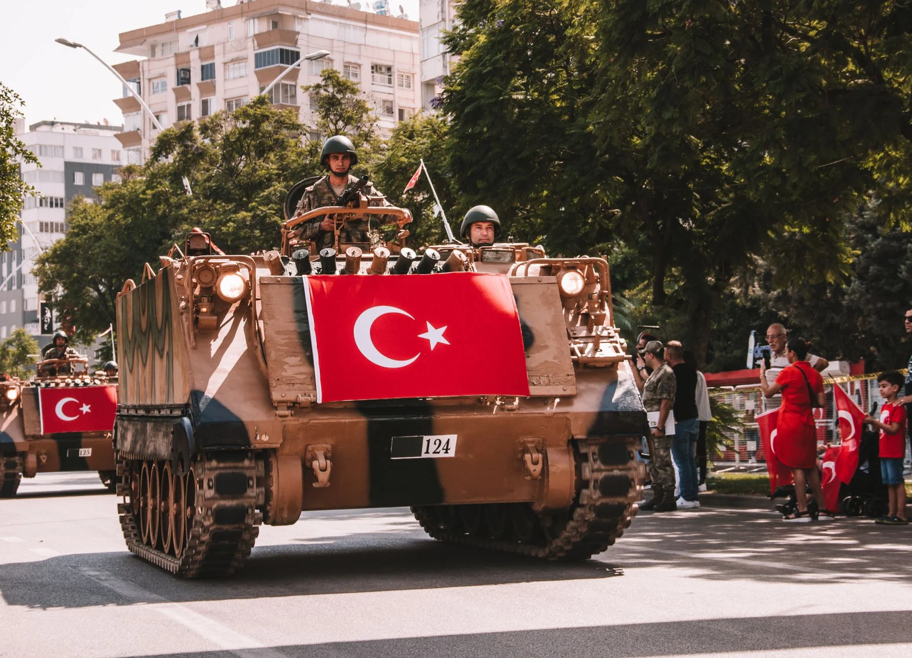 Military tanks in a Turkish parade displaying the national flag and soldiers on a city street.