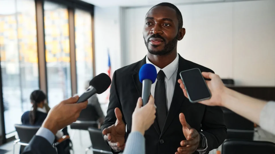 Confident businessman answering questions from the media during a press conference indoors.