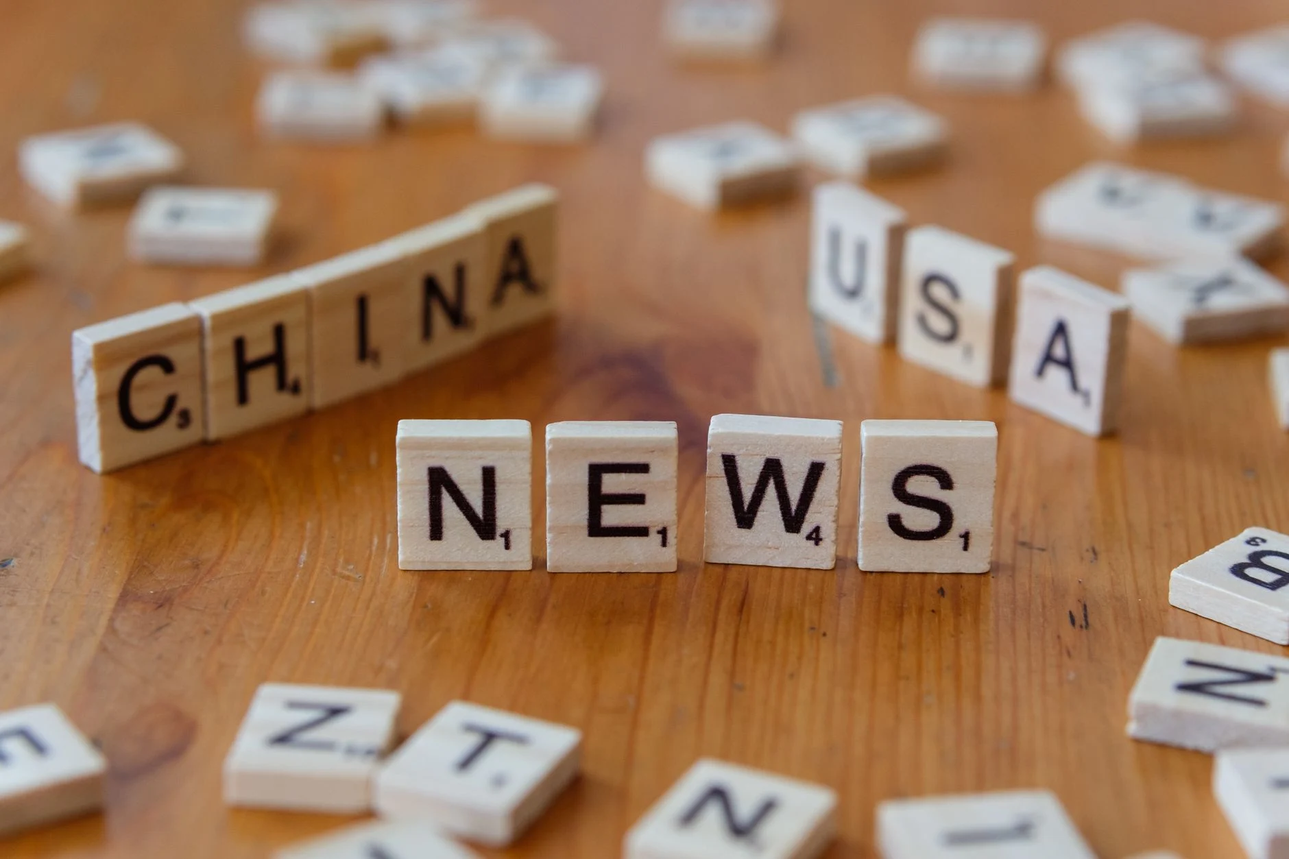 Wooden Scrabble tiles spelling 'NEWS' with 'CHINA' and 'USA' on a wooden surface.