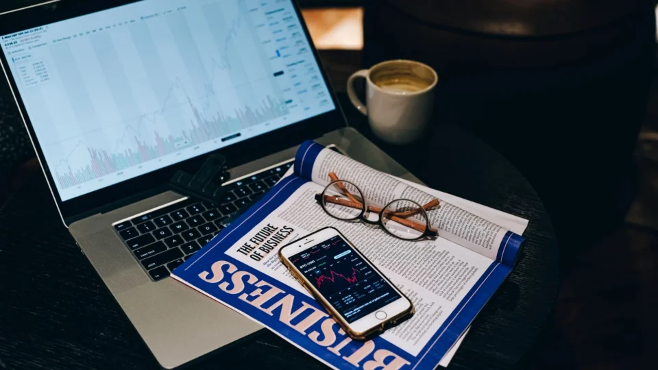A professional workspace featuring a laptop, smartphone, coffee cup, and business magazine on a table.