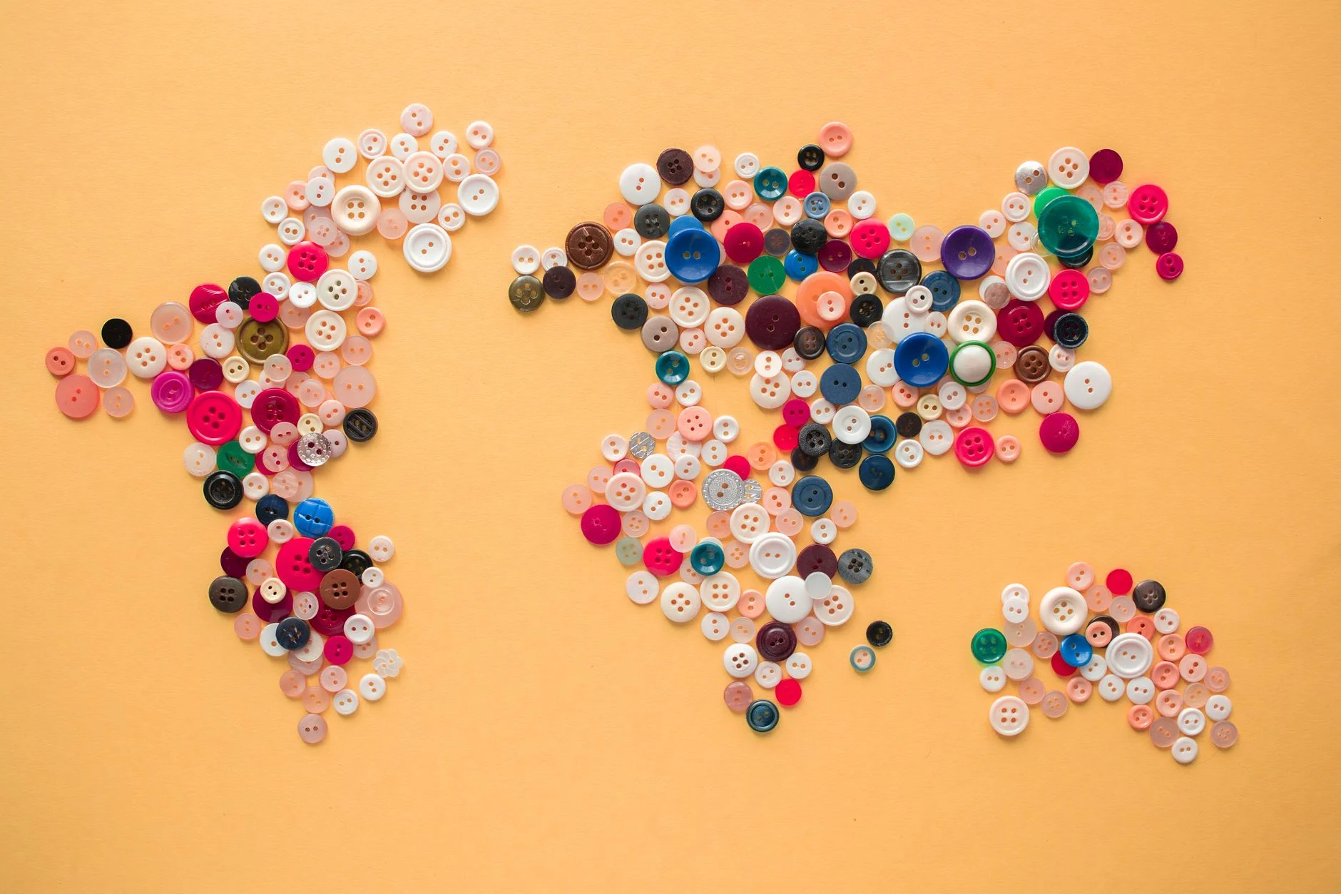 Top view of multicolored buttons of various size arranged on yellow background making world map