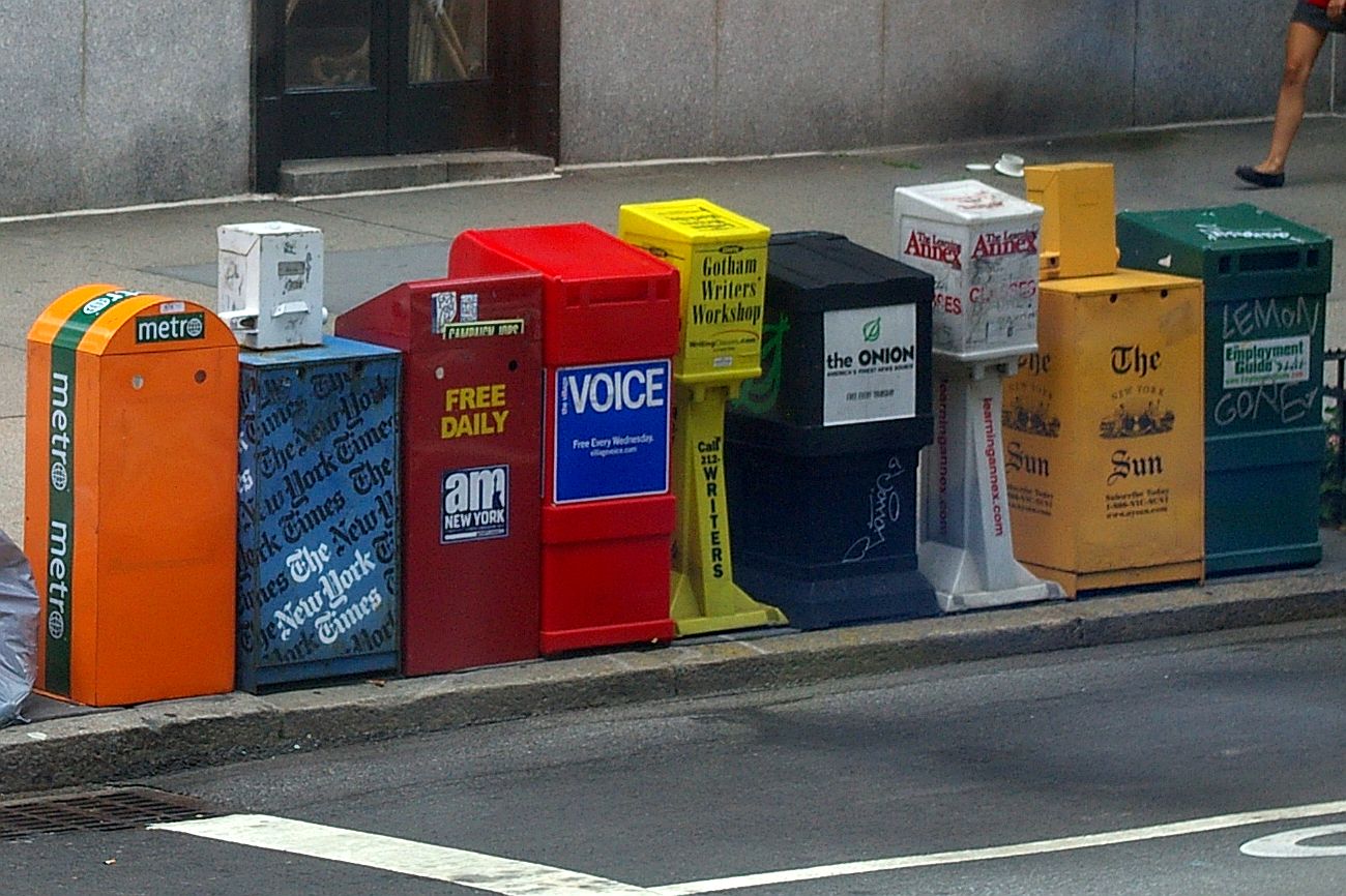 Row of coin-operated newspaper vending machines on a street