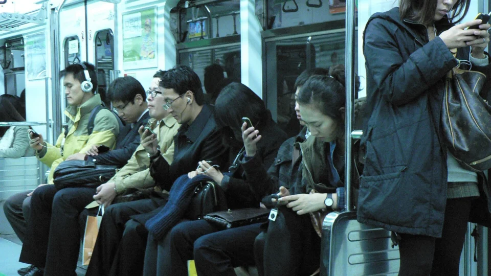 Commuters looking down at smartphones on a metro train