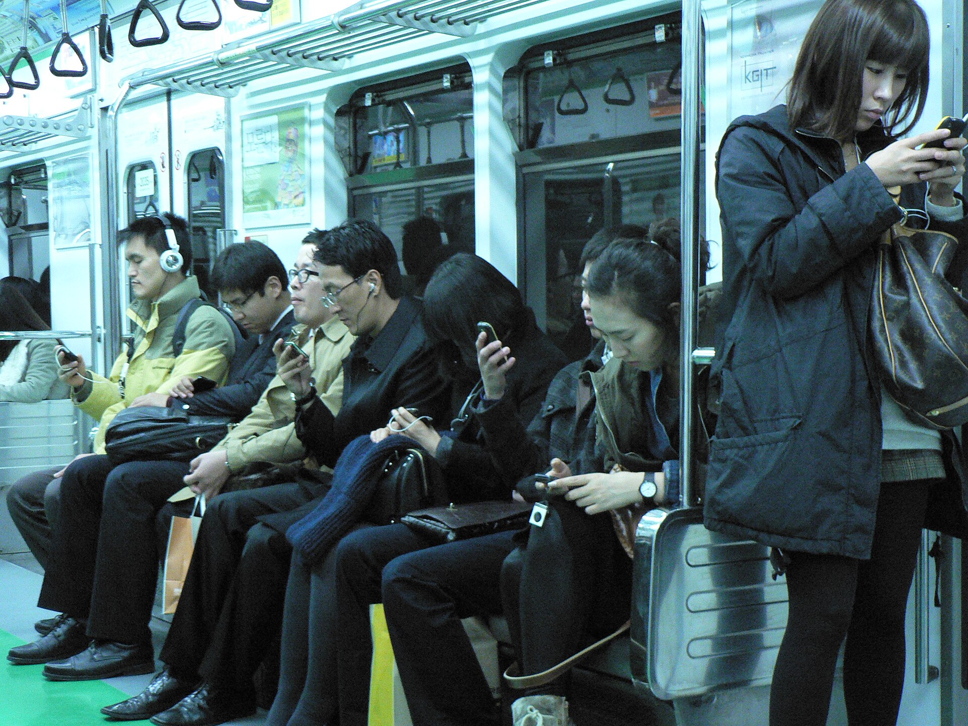 Commuters looking down at smartphones on a metro train