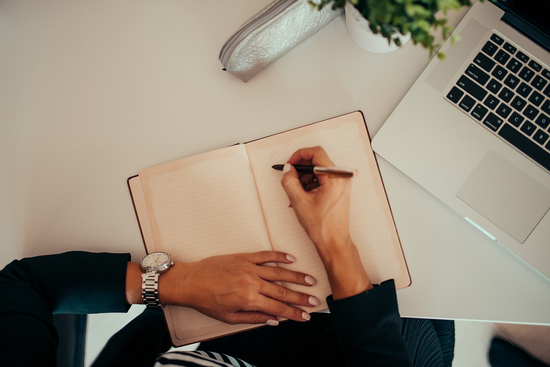 Person writing in a notebook beside a laptop at a desk