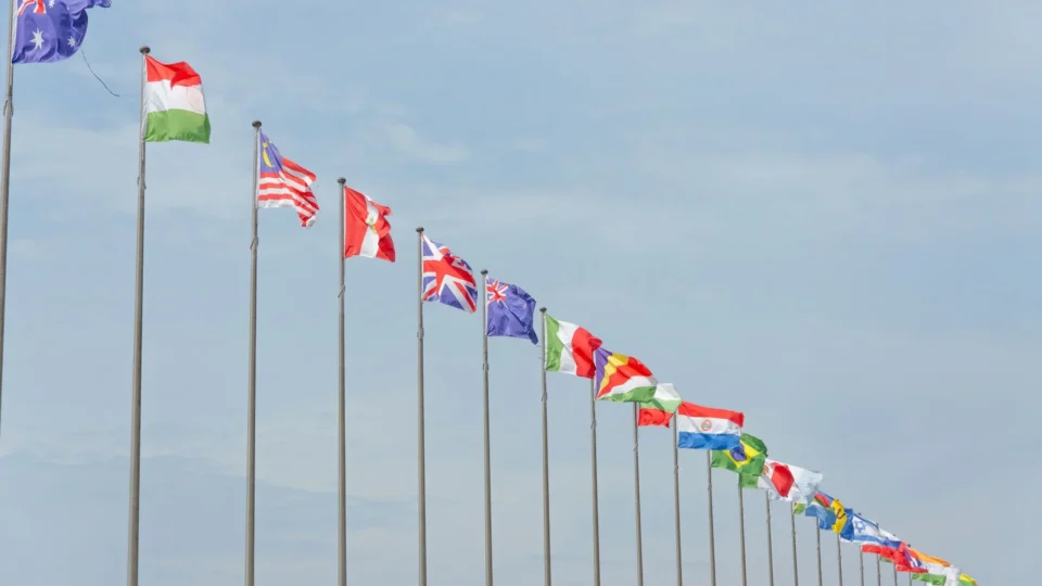 A series of international flags flying in a line against a clear blue sky, symbolizing global unity.