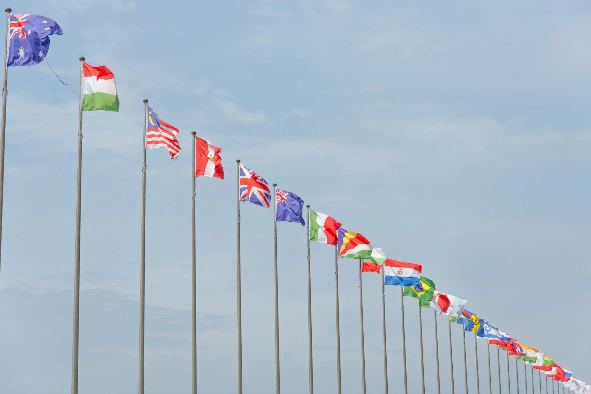 A series of international flags flying in a line against a clear blue sky, symbolizing global unity.