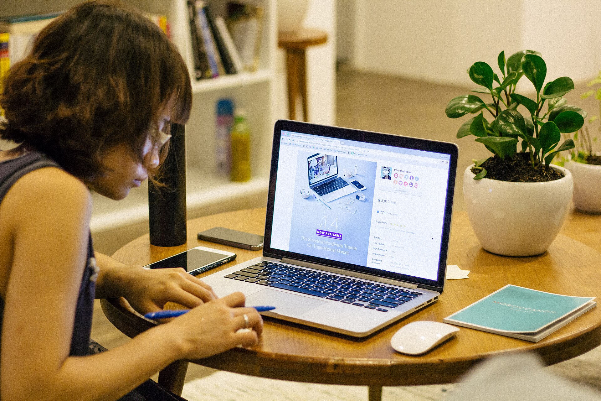 Person taking notes beside a laptop at a coffee table