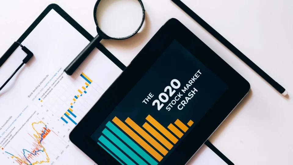 Magnifying glass and tablet analyze 2020 stock market crash data with charts on clipboard.