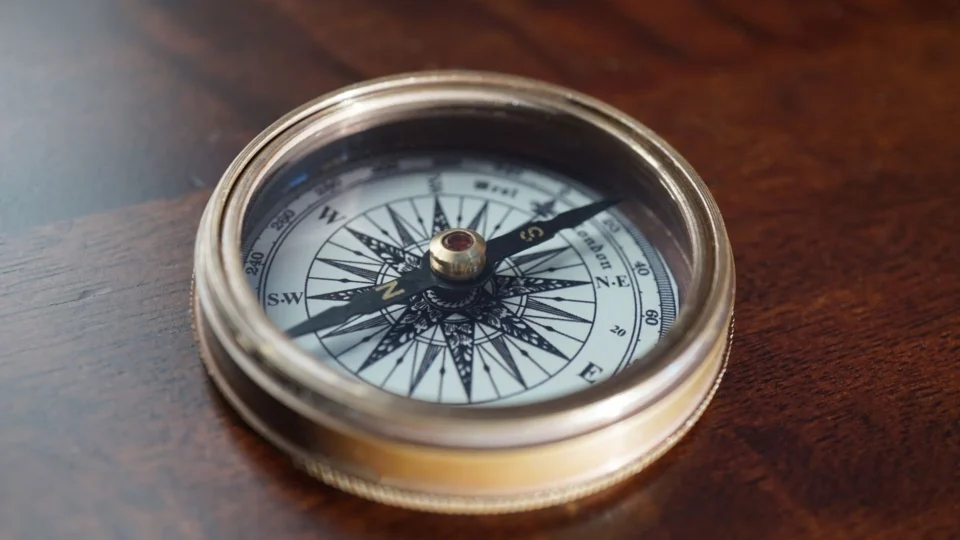 Close-up of a vintage compass resting on a warm, dark wooden surface, indicating navigation and exploration.