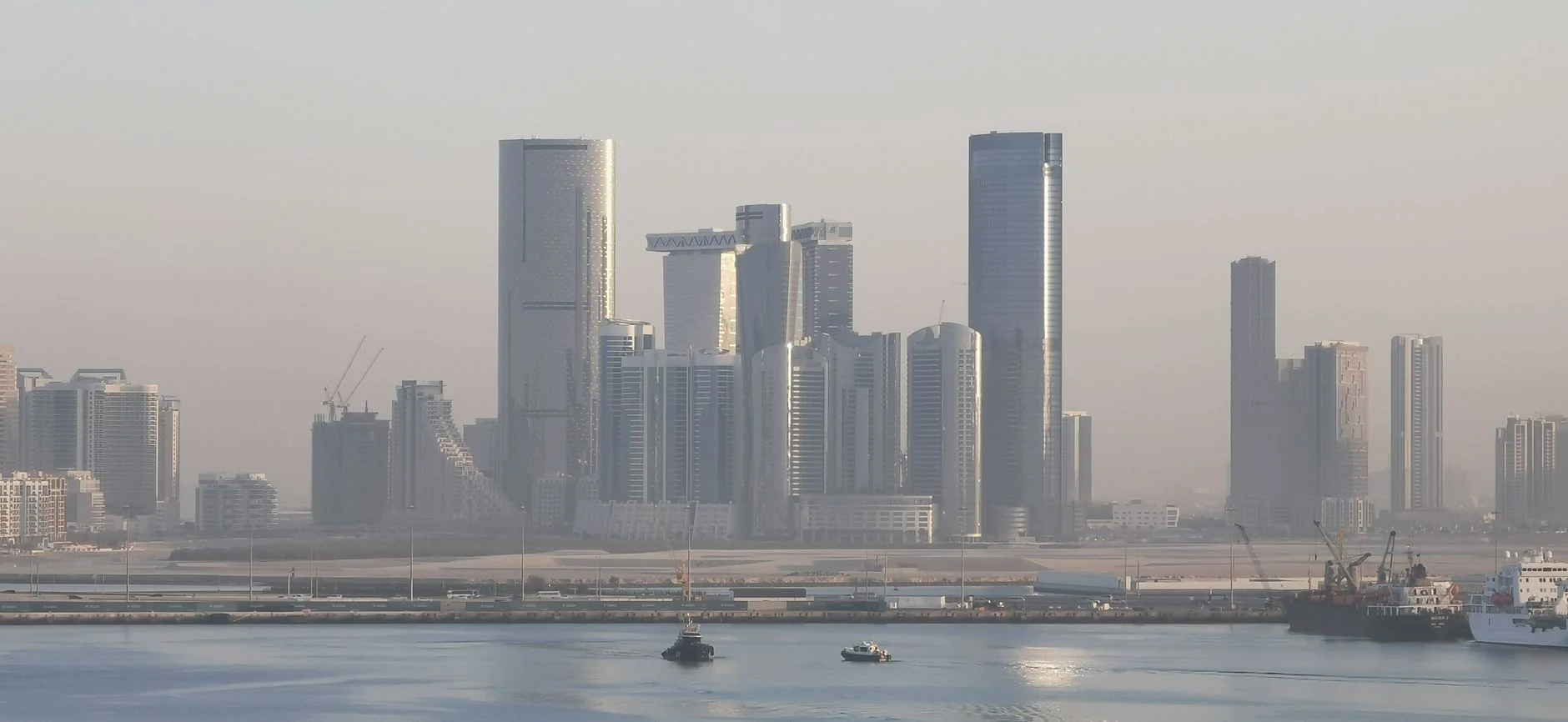 Panoramic view of Abu Dhabi's futuristic skyline with modern skyscrapers under hazy skies.