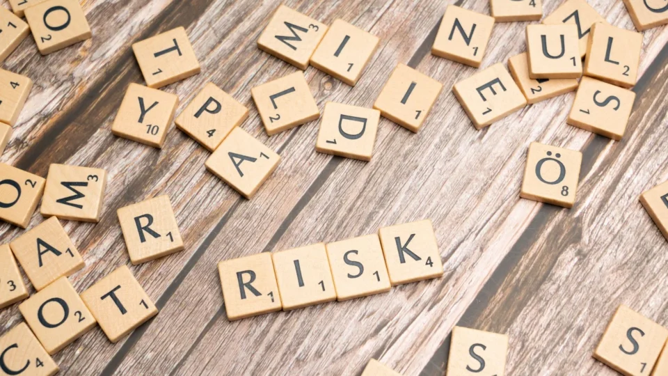 Scrabble tiles spelling out 'risk' scattered on a rustic wooden background, symbolizing uncertainty.
