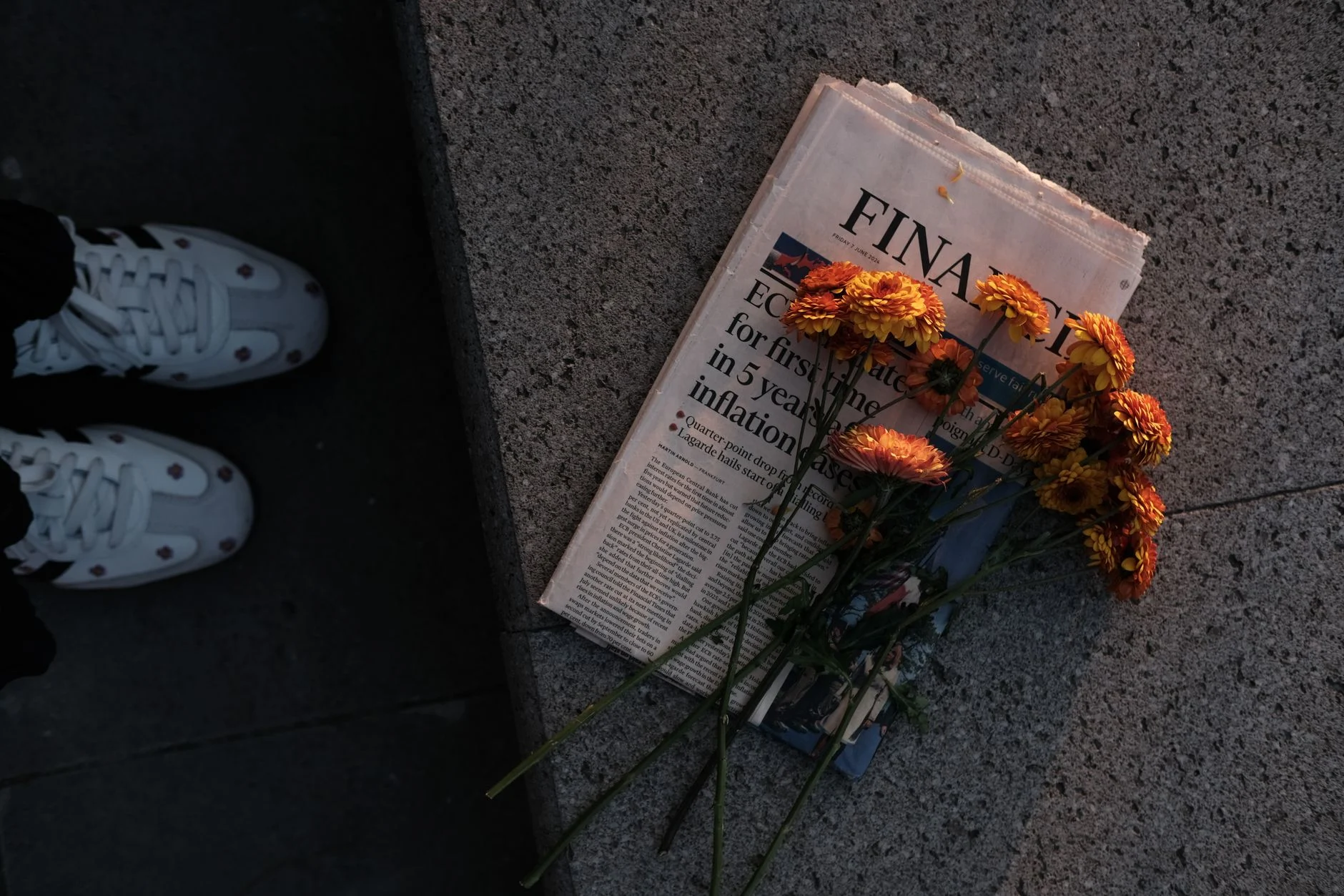 Bouquet of orange flowers atop a financial newspaper in soft evening light.