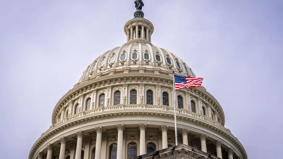 Close-up of the US Capitol dome with the American flag flying against a clear sky.